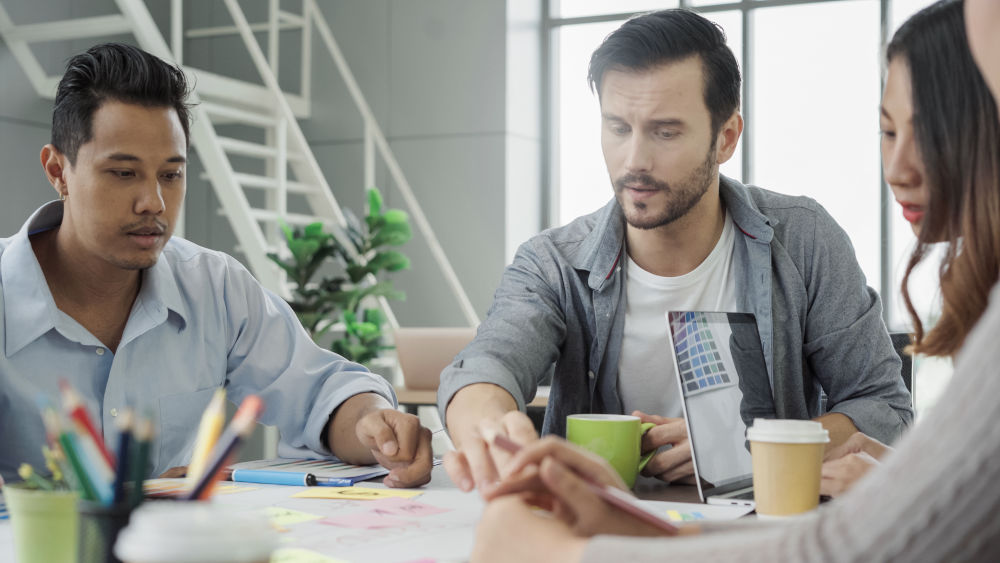 Schulungsraum für Logistik und Verkehr finden: Drei Seminarteilnehmer, zwei Männer und eine Frau, sitzen um einen Tisch herum und lernen gemeinsam.