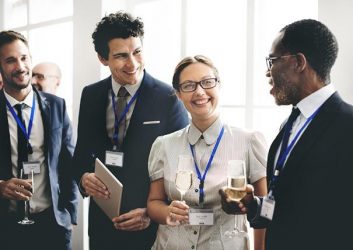 Eine Frau und drei Männer stehen mit Sektgläsern in der Hand auf einem Networking Event zusammen. Sie lächeln und sind in ein angeregtes Gespräch verwickelt.